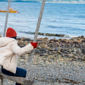 Turista disfrutando de una hamaca frente al Canal Beagle en Puerto Almanza, Tierra del Fuego, con botes pesqueros de fondo.