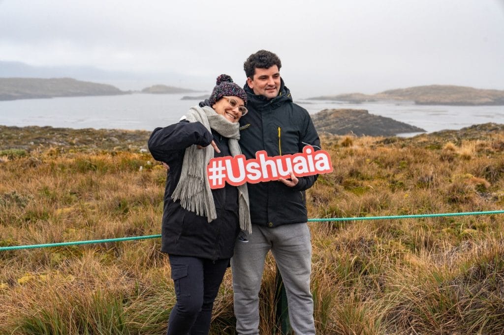 Pareja de turistas posando con el cartel de Ushuaia en el mirador de las Islas Bridges.