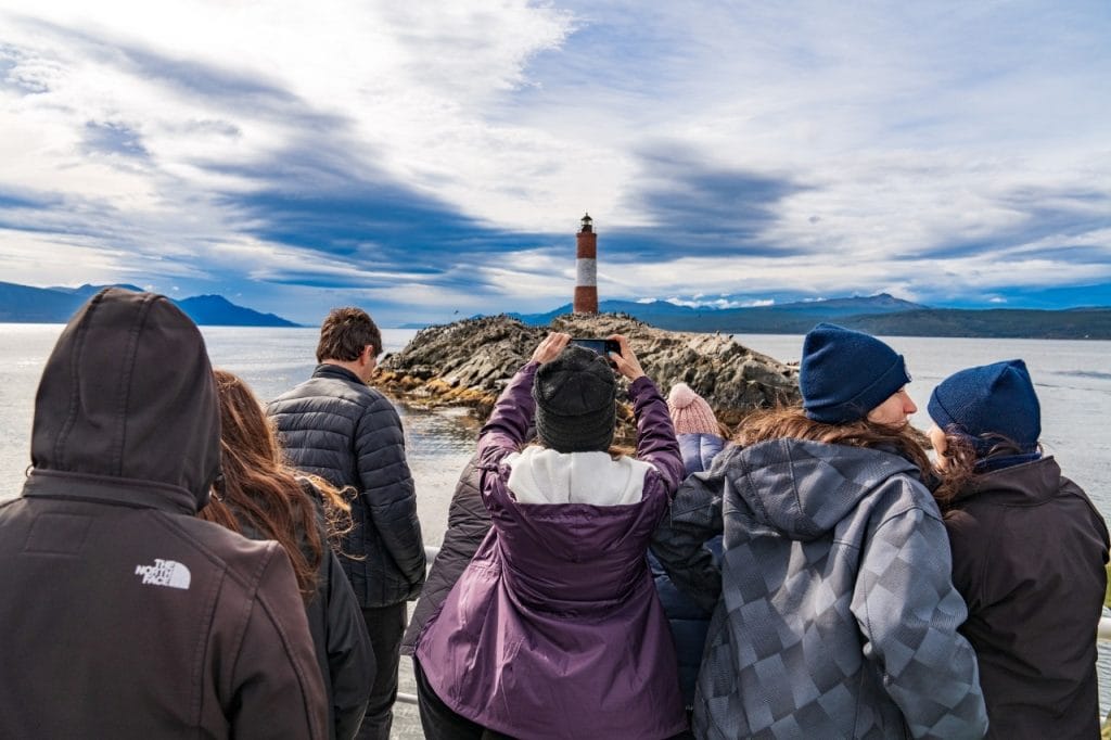 Pasajeros en la cubierta de un catamarán fotografiando el Faro Les Éclaireurs en Ushuaia.