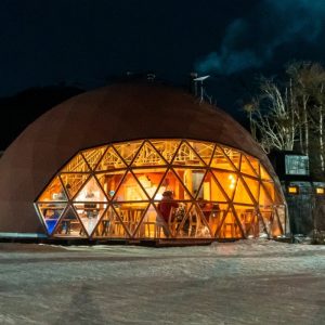 Domo geodésico iluminado en el centro invernal Husky Park en Ushuaia, rodeado de nieve y bosque nativo en plena noche invernal.