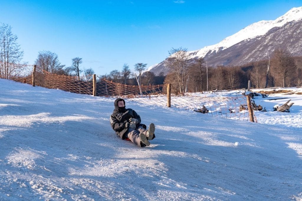 Joven deslizándose en un trineo de plástico por una colina nevada en Park Austral, Ushuaia.