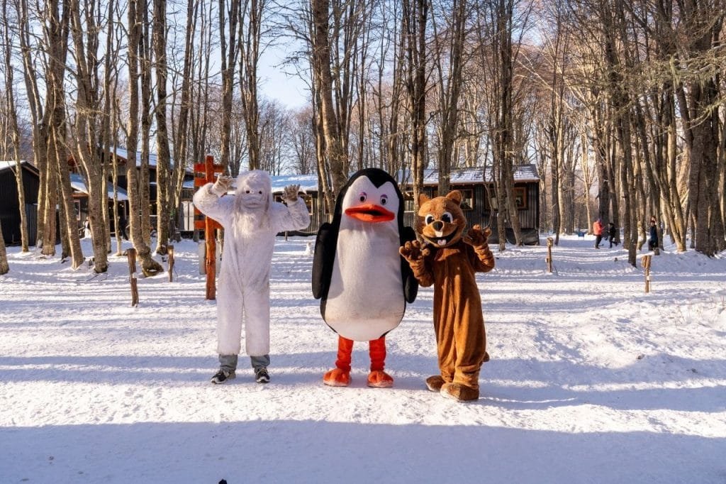 Tres personas disfrazadas de personajes animados en la nieve posando frente a las cabañas de Park Austral.