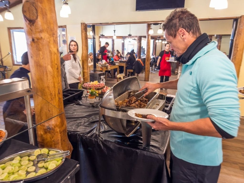 Turista sirviéndose comida caliente en la mesa de buffet del restaurante en Park Austral, Ushuaia.
