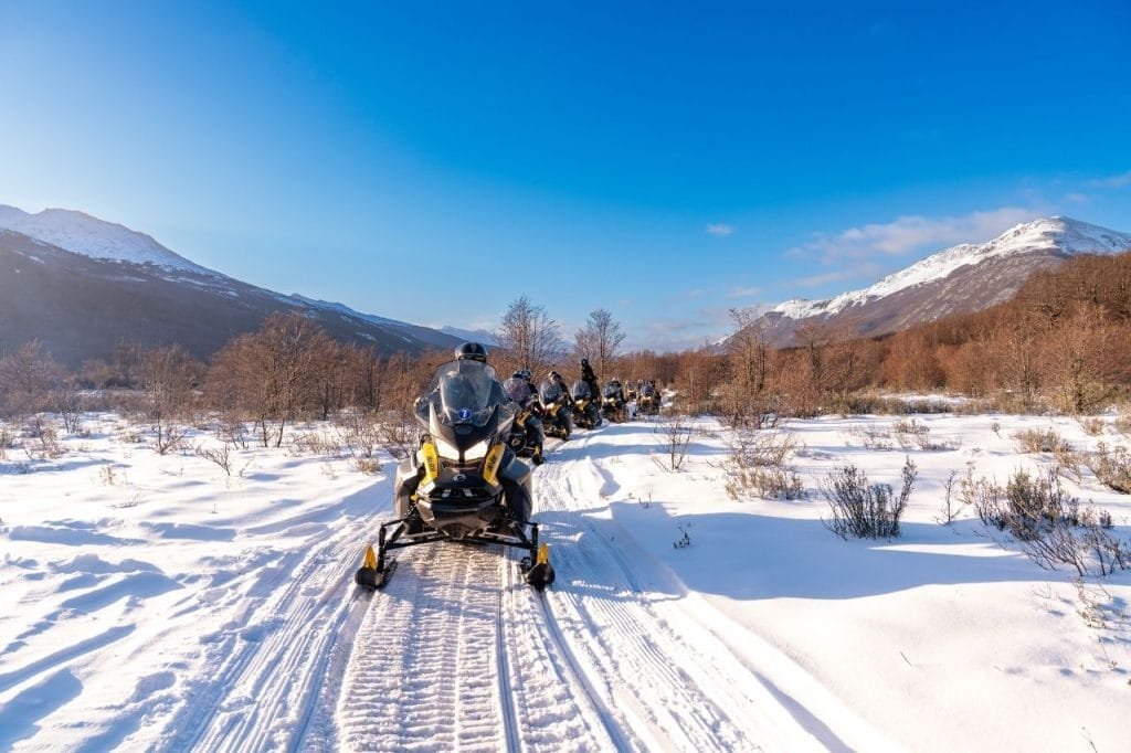 Motos de nieve recorriendo un sendero marcado en la nieve sobre la ladera de una montaña en Park Austral.
