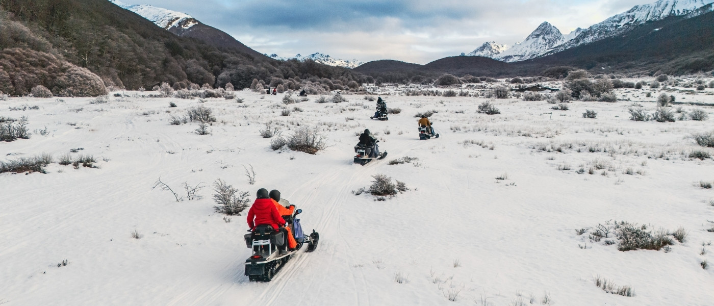 Grupo en motos de nieve recorriendo valle nevado en Ushuaia. Excursión de invierno.