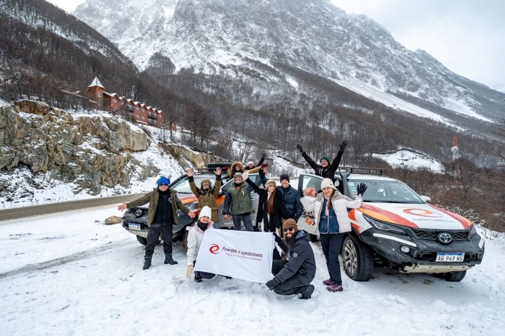 Grupo de turistas posando junto a camionetas 4x4 en la nieve con bandera de Aswanek Expediciones en Ushuaia.