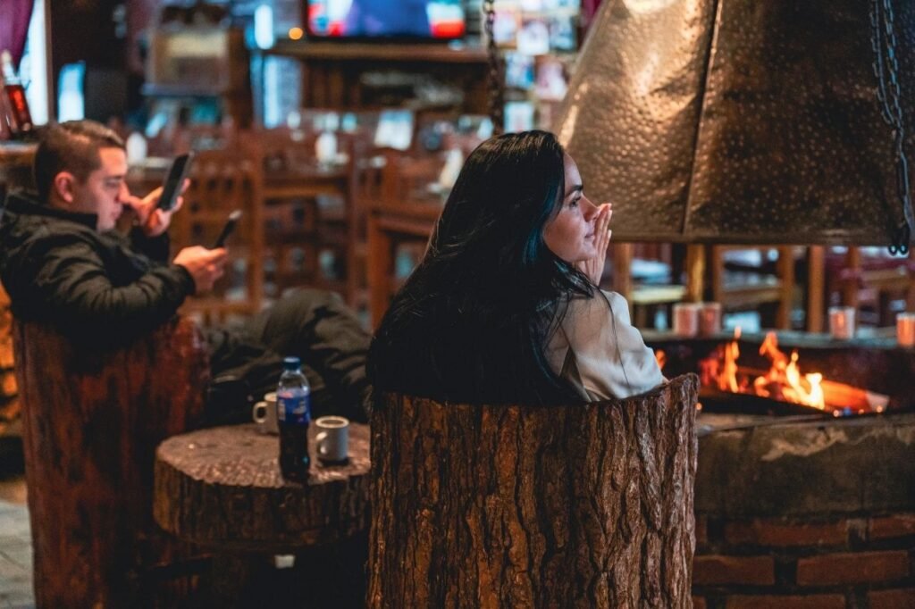 Mujer sentada en un taburete de tronco junto al hogar a leña encendido en el Centro Invernal Las Cotorras, Ushuaia.