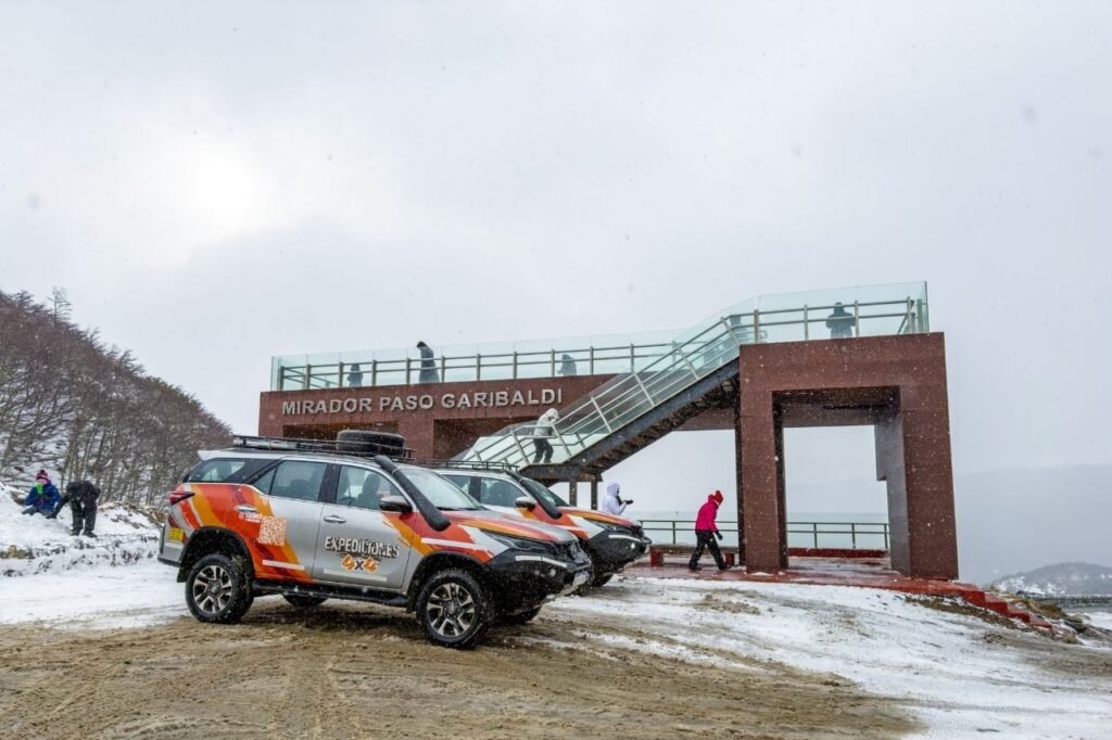 Camionetas 4x4 de expedición estacionadas frente a la estructura del Mirador Paso Garibaldi en la nieve.