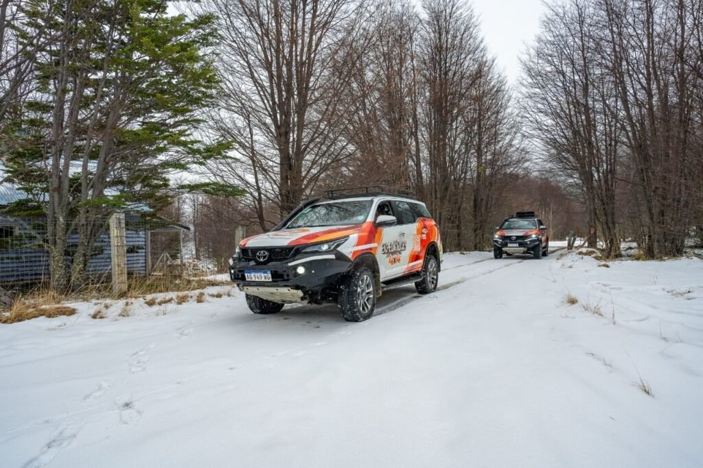 Camioneta 4x4 de turismo transitando por un camino cubierto de nieve en medio de un bosque en Ushuaia.