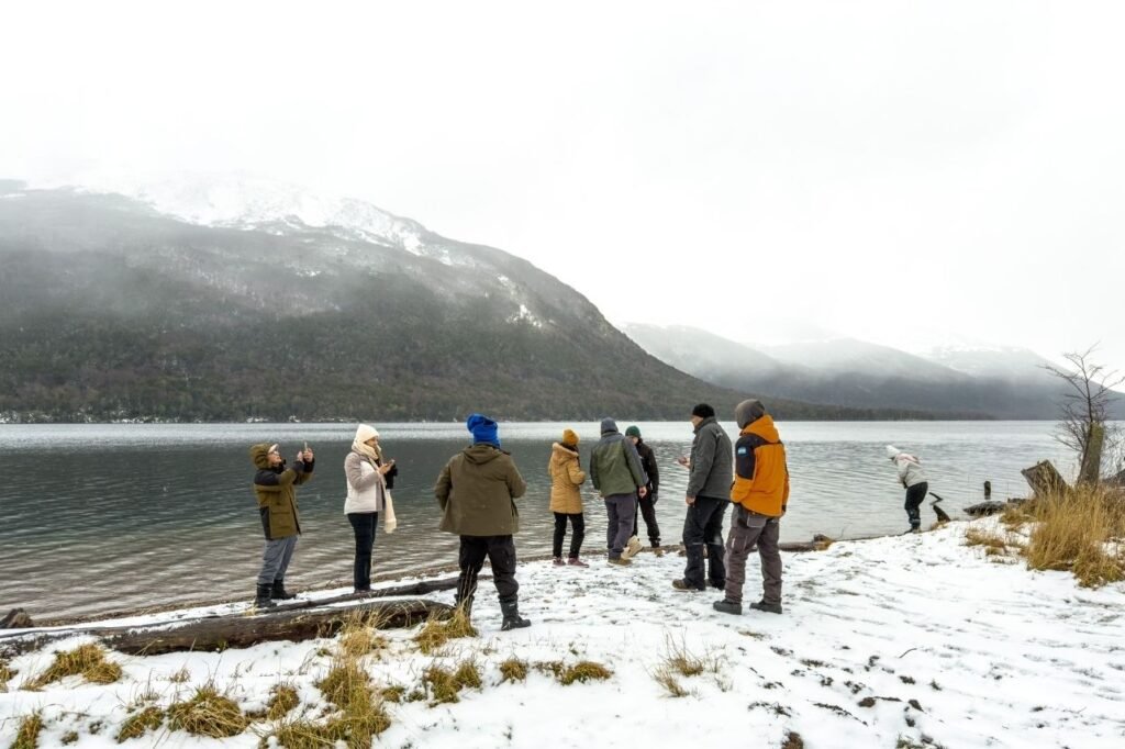 Grupo de viajeros contemplando el paisaje nevado a orillas de un lago en Tierra del Fuego.