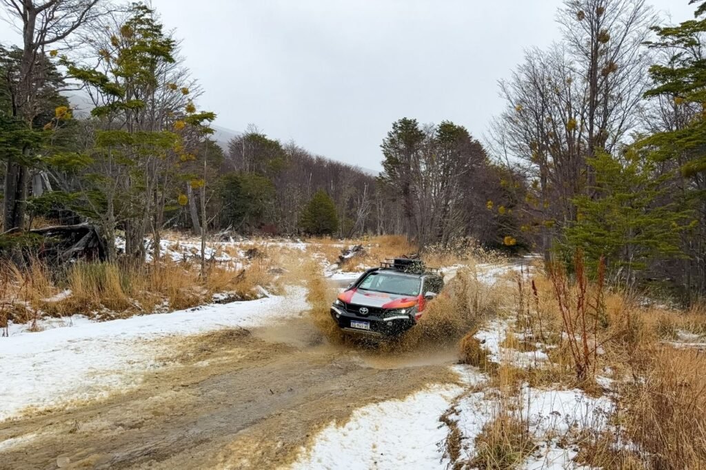 Camioneta 4x4 atravesando a velocidad un vado de barro salpicando en el bosque patagónico.