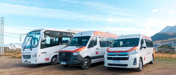 Flota de vehículos de transporte de la agencia Aswalek en Ushuaia, que incluye un minibús Agrale, un furgón Mercedes-Benz Sprinter y una minivan Toyota Hiace, estacionados frente a montañas nevadas.