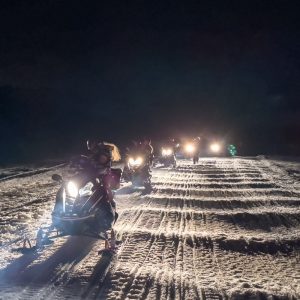 Grupo de personas conduciendo motos de nieve, por la noche en un sendero del valle de Tierra Mayor en el centro invernal Husky Park.