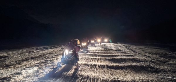 Grupo de personas conduciendo motos de nieve, por la noche en un sendero del valle de Tierra Mayor en el centro invernal Husky Park.