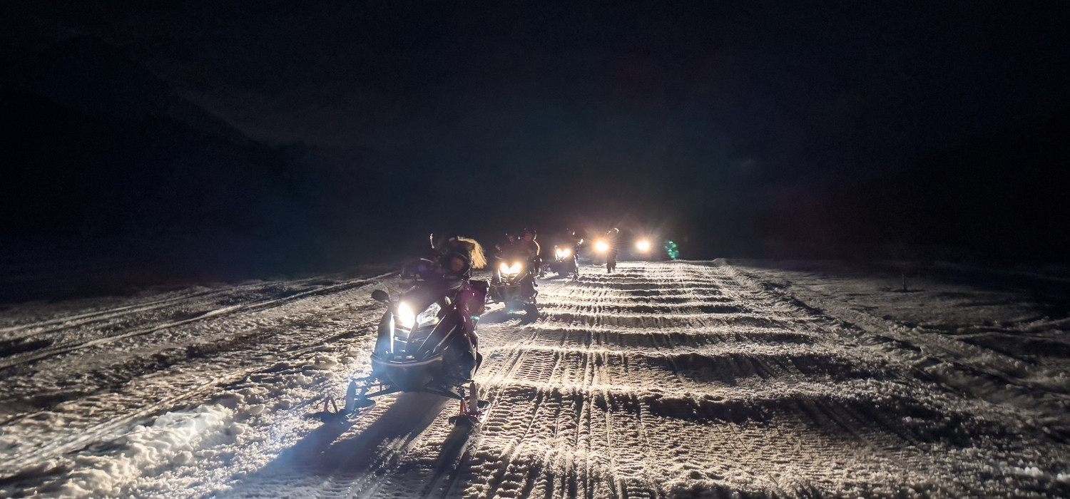 Grupo de personas conduciendo motos de nieve, por la noche en un sendero del valle de Tierra Mayor en el centro invernal Husky Park.