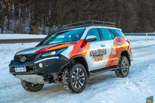 Una camioneta Toyota SW4 blanca de expedición 4x4, equipada con parachoques reforzado negro, snorkel y portaequipajes de techo con el logo de Aswalek Expediciones, estacionada en un camino de nieve profunda en un valle andino de Ushuaia.