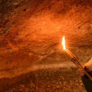 Guía de turismo iluminando pinturas rupestres con una antorcha dentro de una cueva.