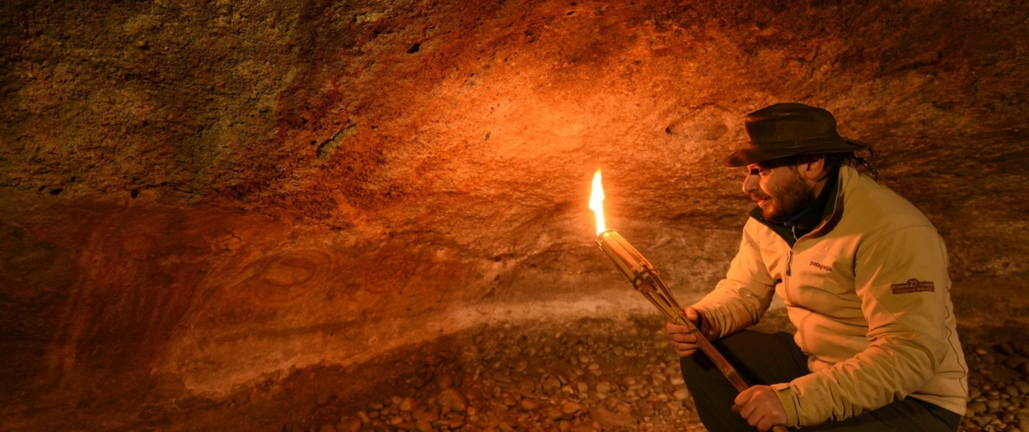 Guía de turismo iluminando pinturas rupestres con una antorcha dentro de una cueva.