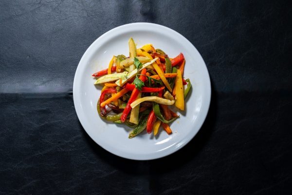 Plato de vegetales salteados con morrón rojo, amarillo, verde y zucchini en fondo oscuro.