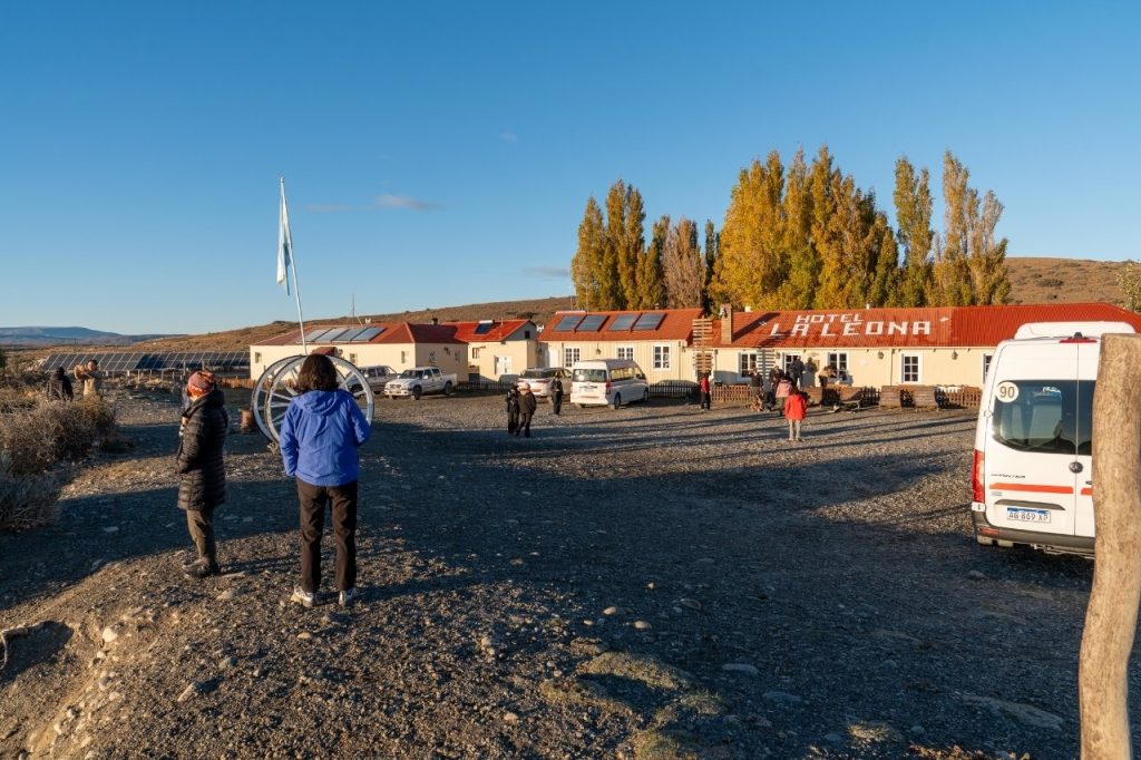 Fachada del histórico Hotel La Leona con su techo rojo, paneles solares y turistas junto a camionetas de excursión en un día soleado.