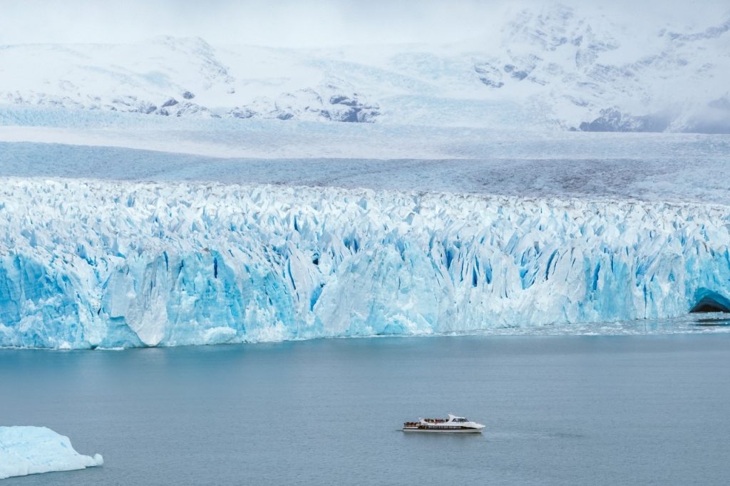 Barco de excursión navegando en las aguas del Lago Argentino frente a la imponente pared de hielo azul del Glaciar Perito Moreno.