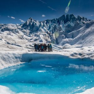 Un grupo de turistas realizando minitrekking sobre el hielo blanco junto a un piletón natural de agua turquesa en el Glaciar Perito Moreno.
