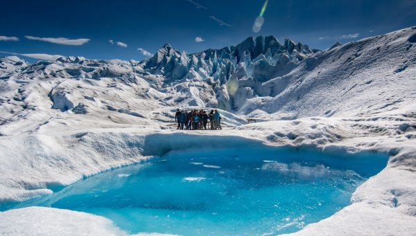 Un grupo de turistas realizando minitrekking sobre el hielo blanco junto a un piletón natural de agua turquesa en el Glaciar Perito Moreno.
