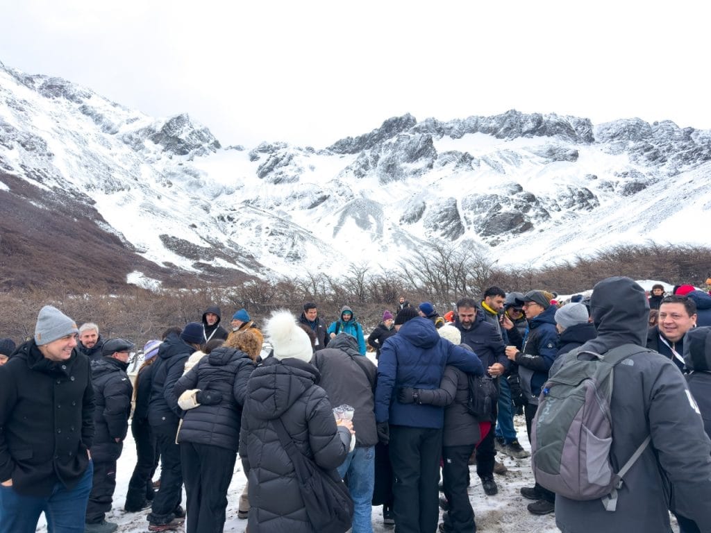 Un grupo de turistas con ropa de invierno de pie en la nieve al pie del Glaciar Martial, con imponentes montañas andinas nevadas al fondo, Ushuaia.