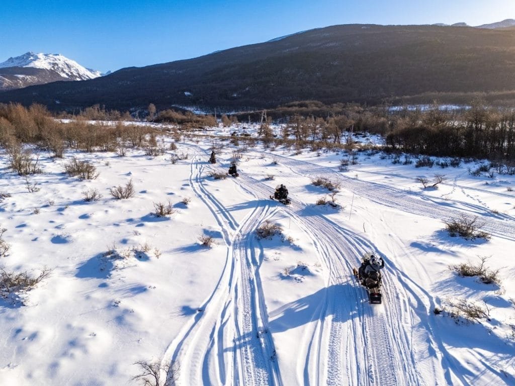 Vista aérea de una larga fila de motos de nieve atravesando un paisaje nevado en el Park Austral, Ushuaia, durante el invierno.